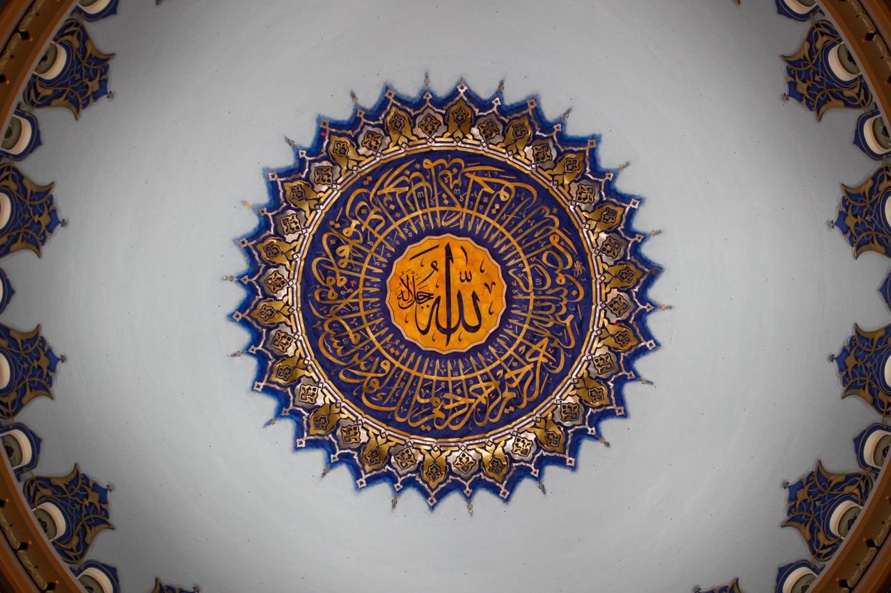 Detailed view of a beautifully decorated mosque dome ceiling in İstanbul, showcasing Islamic art and Arabic calligraphy.