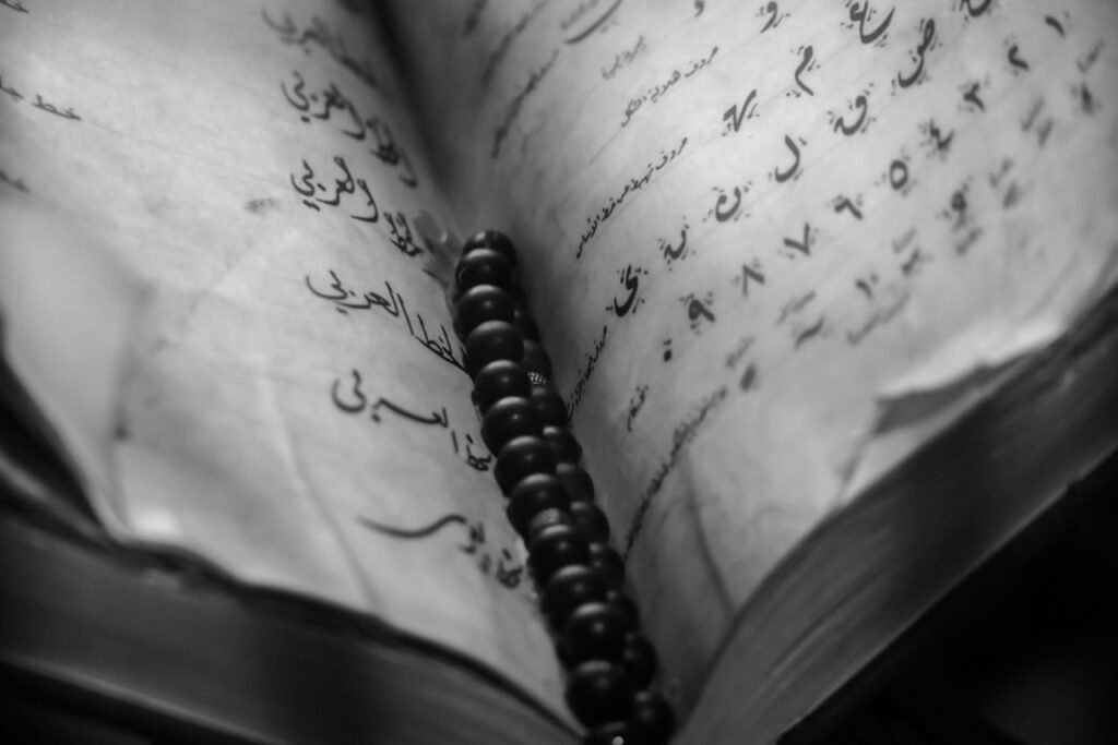 Black and white photo of an open Arabic book with beads, capturing cultural and spiritual essence.